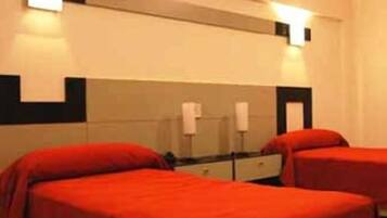 A hotel room with two beds, each with red bedding, a bedside table, and a mirror.