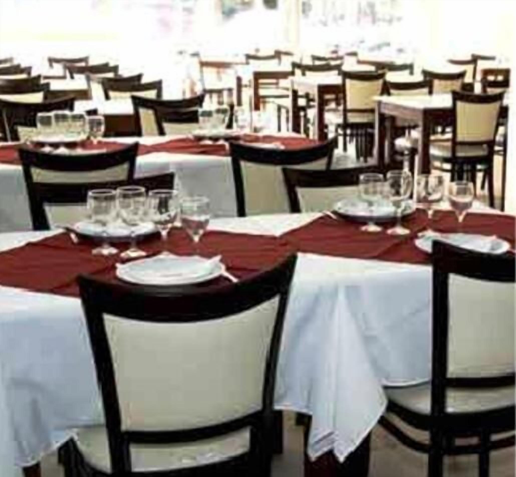 A restaurant with tables set for dining, featuring white tablecloths and dark chairs.