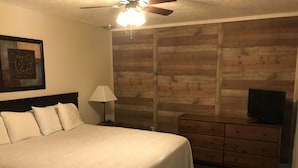 Une chambre d’hôtel avec un grand lit, un panneau mural en bois, un téléviseur posé sur une commode et un ventilateur de plafond.