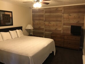 A hotel room with a large bed, a wooden wall panel, a TV on a dresser, and a ceiling fan. - Carriage House Country Club (Pocono Manor)