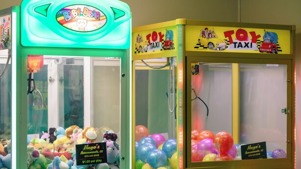 A row of brightly lit claw machines with plush toys and balloons inside. - Carriage House Country Club (Pocono Manor)