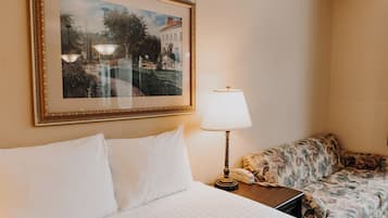 A hotel room with a bed, a framed landscape painting, a lamp, and a floral sofa.