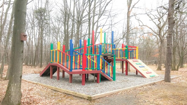 Un terrain de jeux avec des structures colorées, situé dans un parc arboré.