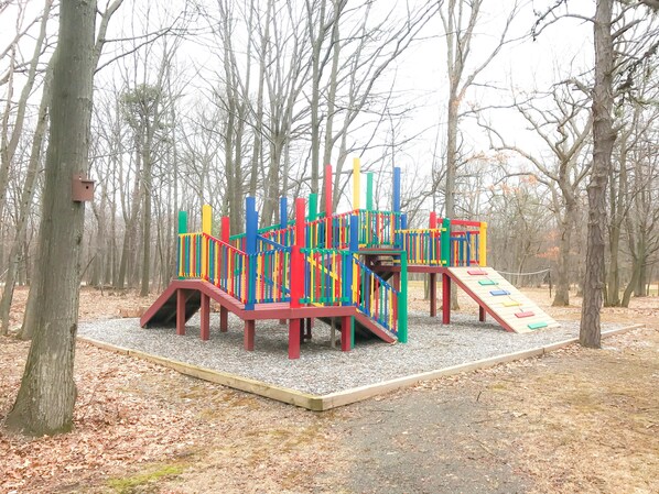 A playground with colorful play structures in a wooded park area. - Carriage House Country Club (Pocono Manor)