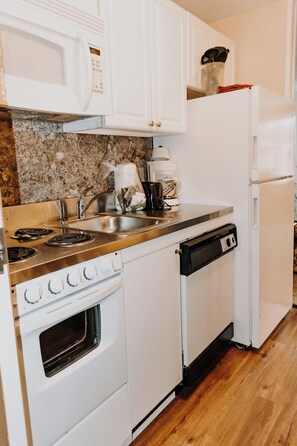 A compact kitchen with white appliances, including a stove, oven, dishwasher, and refrigerator. - Carriage House Country Club (Pocono Manor)