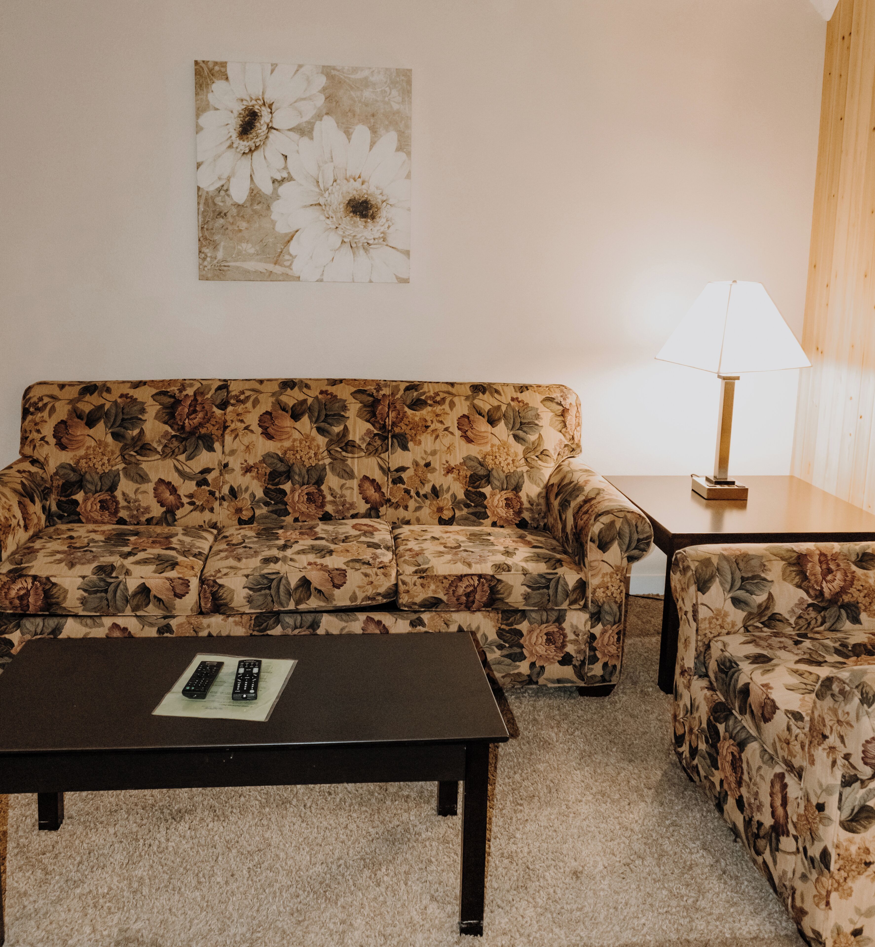 Un salón con un sofá floral, un sillón a juego, una mesa de centro y una lámpara.