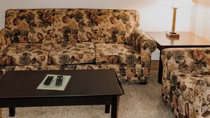 A living room with a floral sofa, a matching armchair, a coffee table, and a lamp. - Carriage House Country Club (Pocono Manor)