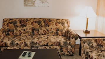 A living room with a floral sofa, a matching armchair, a coffee table, and a lamp.