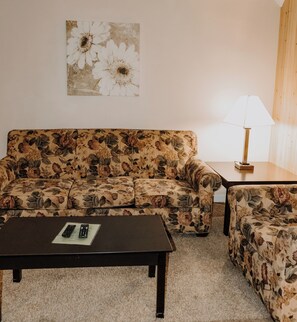 A living room with a floral sofa, a matching armchair, a coffee table, and a lamp.