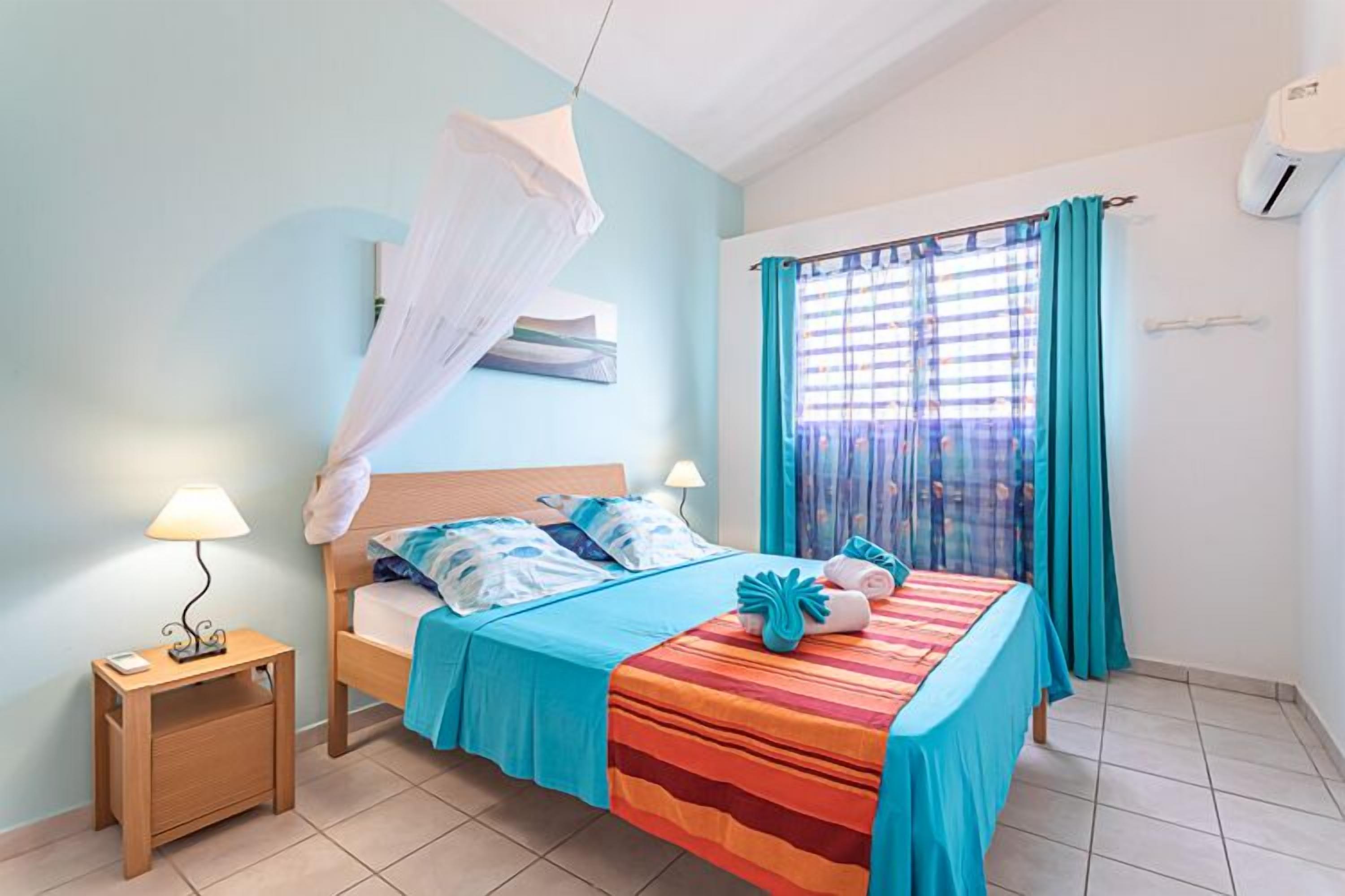 A bedroom with a bed, bedside tables, a mosquito net, curtains, and a window.