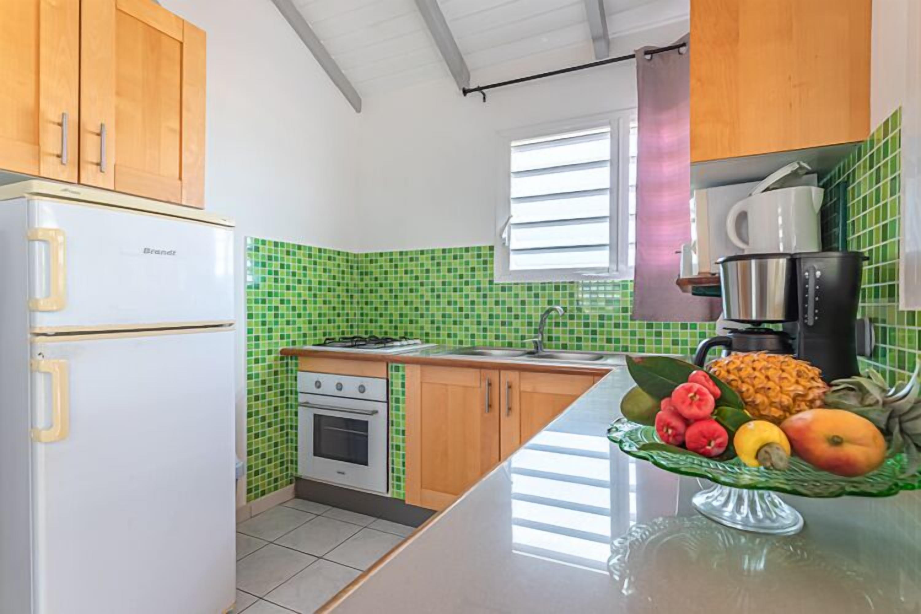 A kitchen with a refrigerator, stove, sink, and a fruit bowl on the counter.