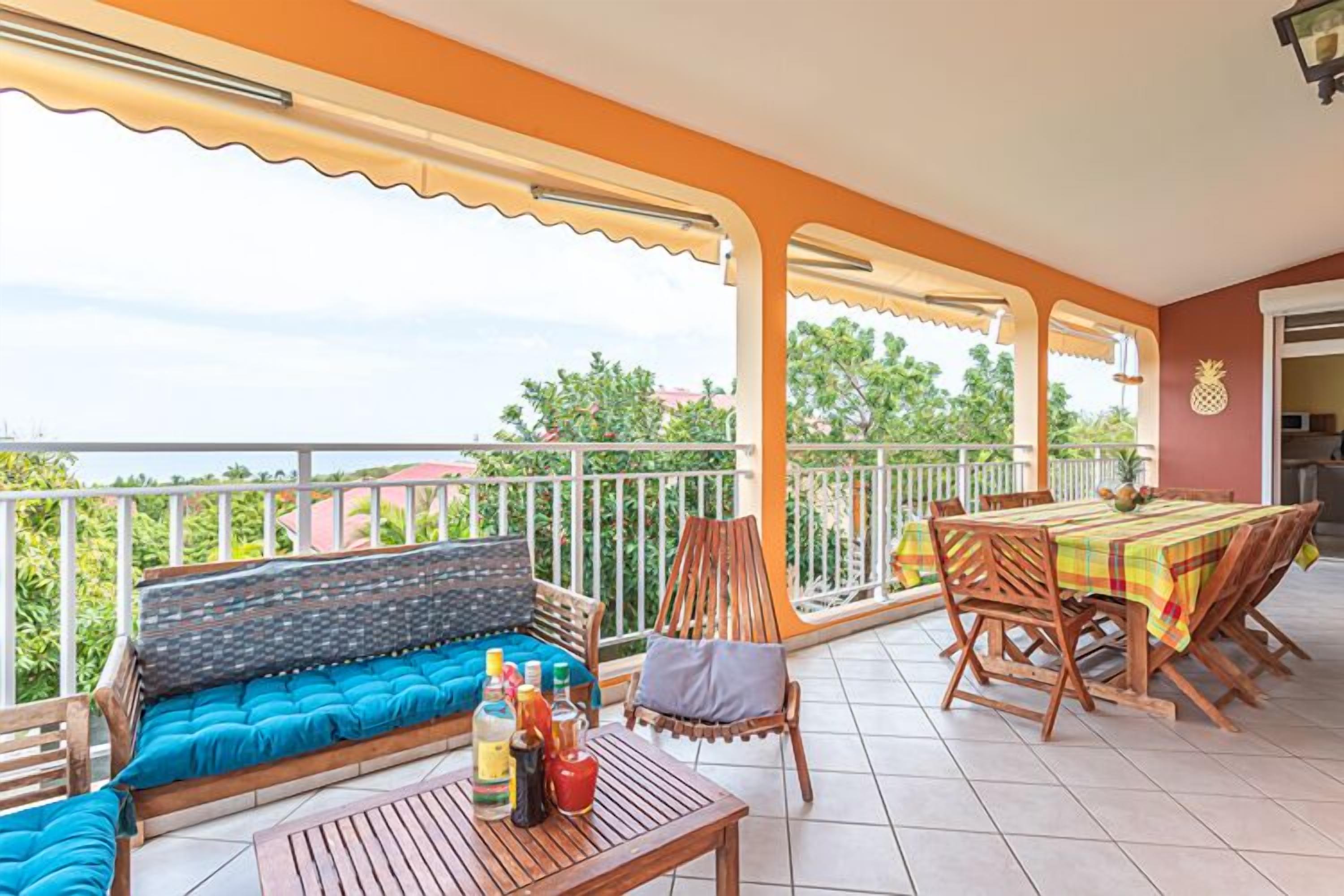 A balcony with a wooden table, chairs, and a sofa with blue cushions.
