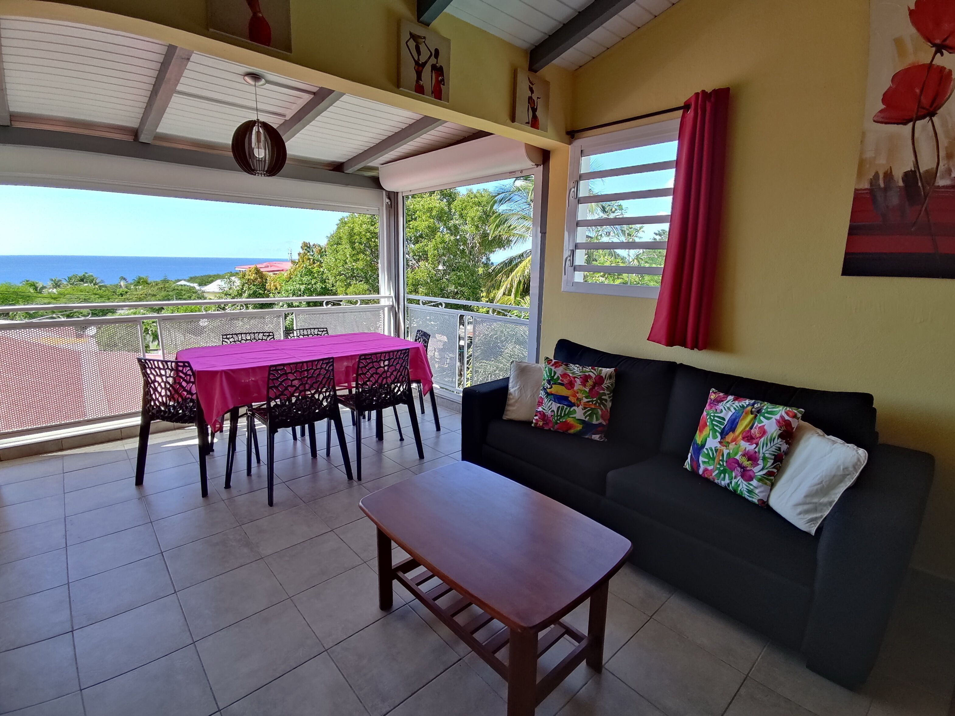 Un balcón con mesa y sillas, un sofá con cojines estampados y vistas al mar.
