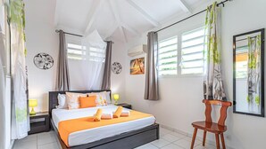 Un dormitorio con cama, dos mesitas de noche, una silla y un ventanal con cortinas.