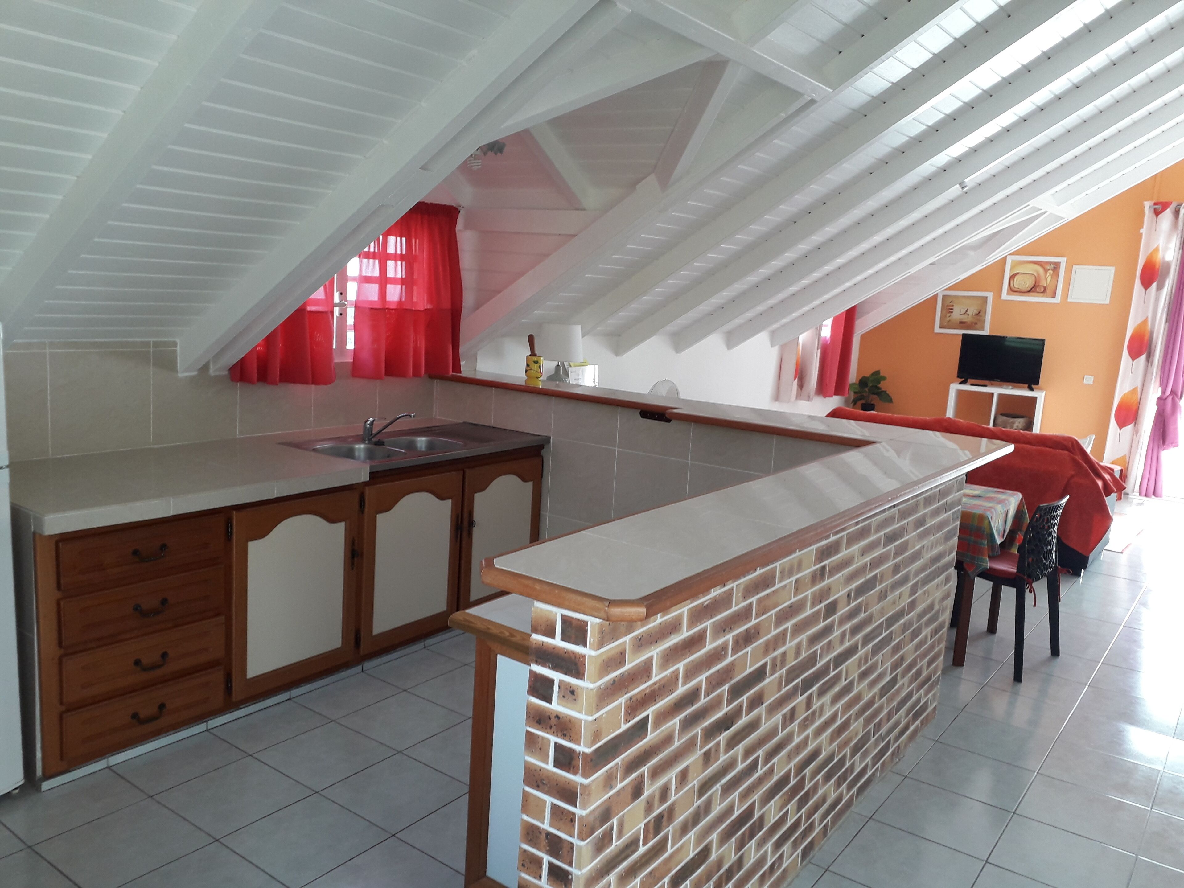 A kitchen with a brick island, wooden cabinets, and a red curtain.
