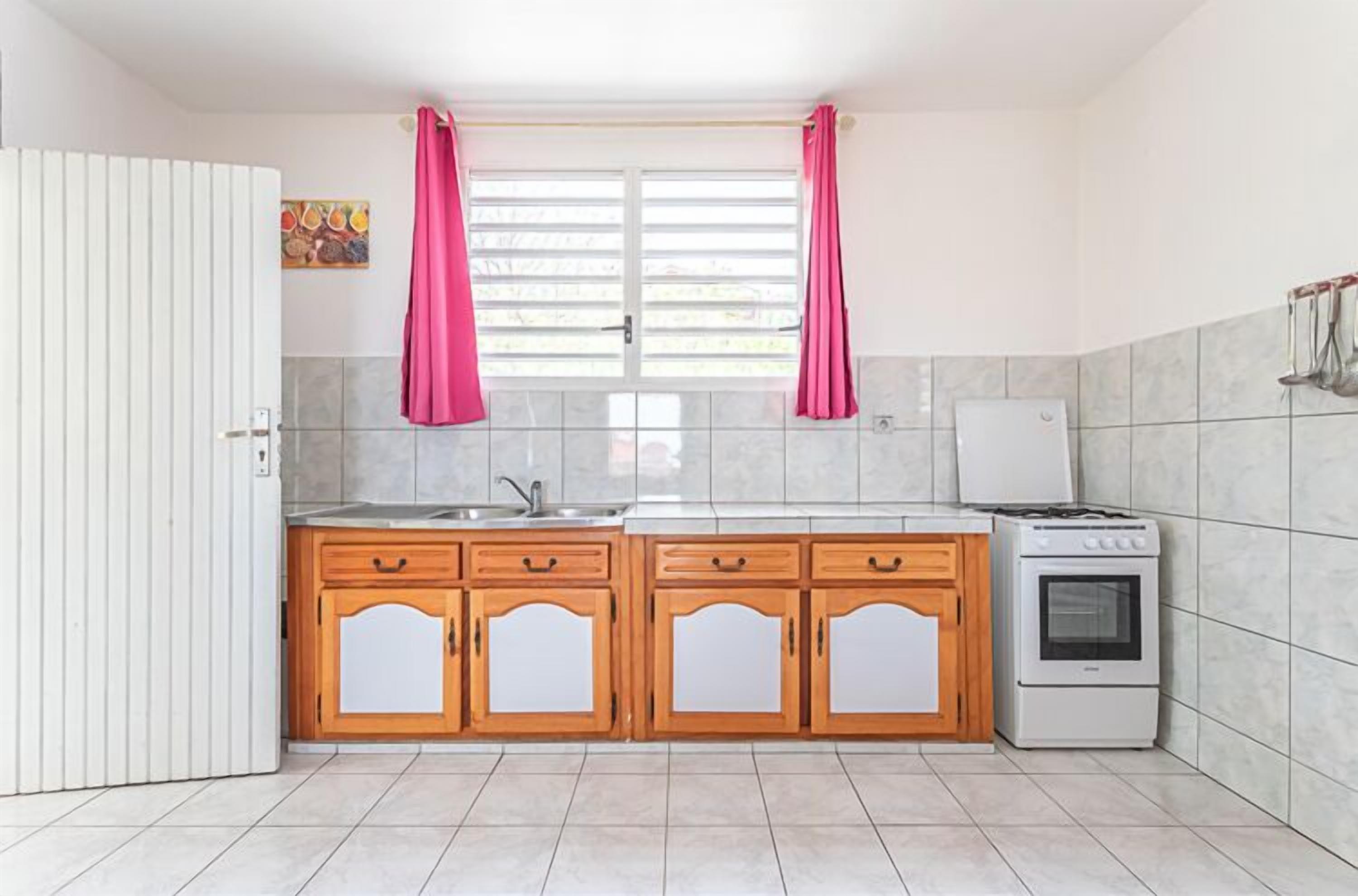 A kitchen with wooden cabinets, a stove, and a window with curtains.