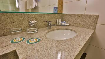 A bathroom with a granite countertop, a white sink, a glass shelf above the sink, and a towel rack.