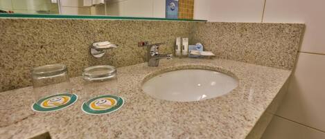 A bathroom with a granite countertop, a white sink, a glass shelf above the sink, and a towel rack.