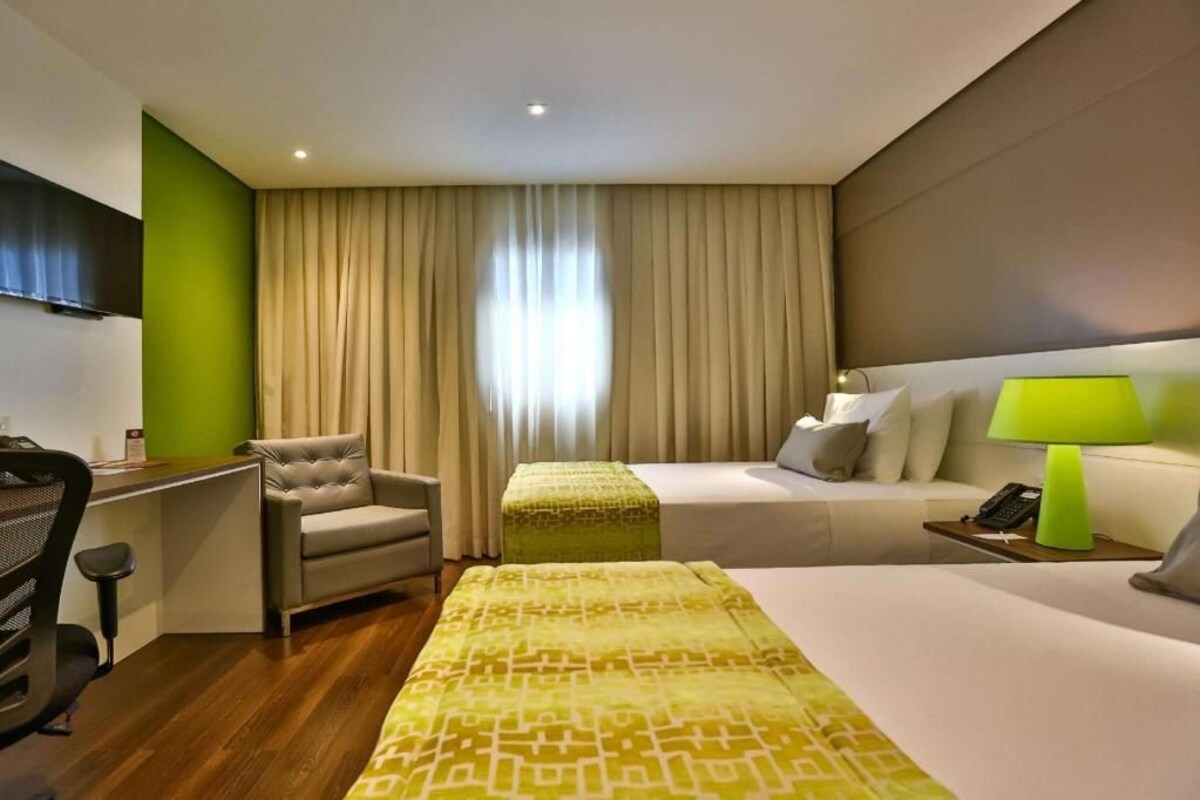 A hotel room with a bed, a desk, a chair, a TV, and a window with curtains.
