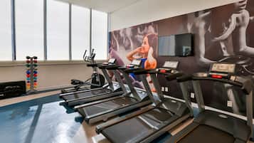 Un gimnasio con cintas de correr, máquinas de pesas y una pared con carteles de fitness.