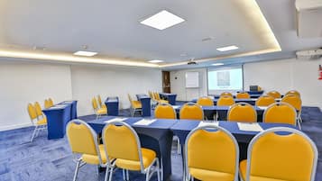 Ein Konferenzraum mit Tischen, Stühlen, einer Projektionsfläche und einer Whiteboard-Tafel.