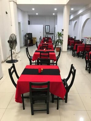 A long dining area with tables covered in red tablecloths and black chairs. - Hotel Zenú (Montería)