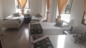 Une chambre d’hôtel avec deux lits simples, une petite table, une chaise et une fenêtre avec des rideaux.