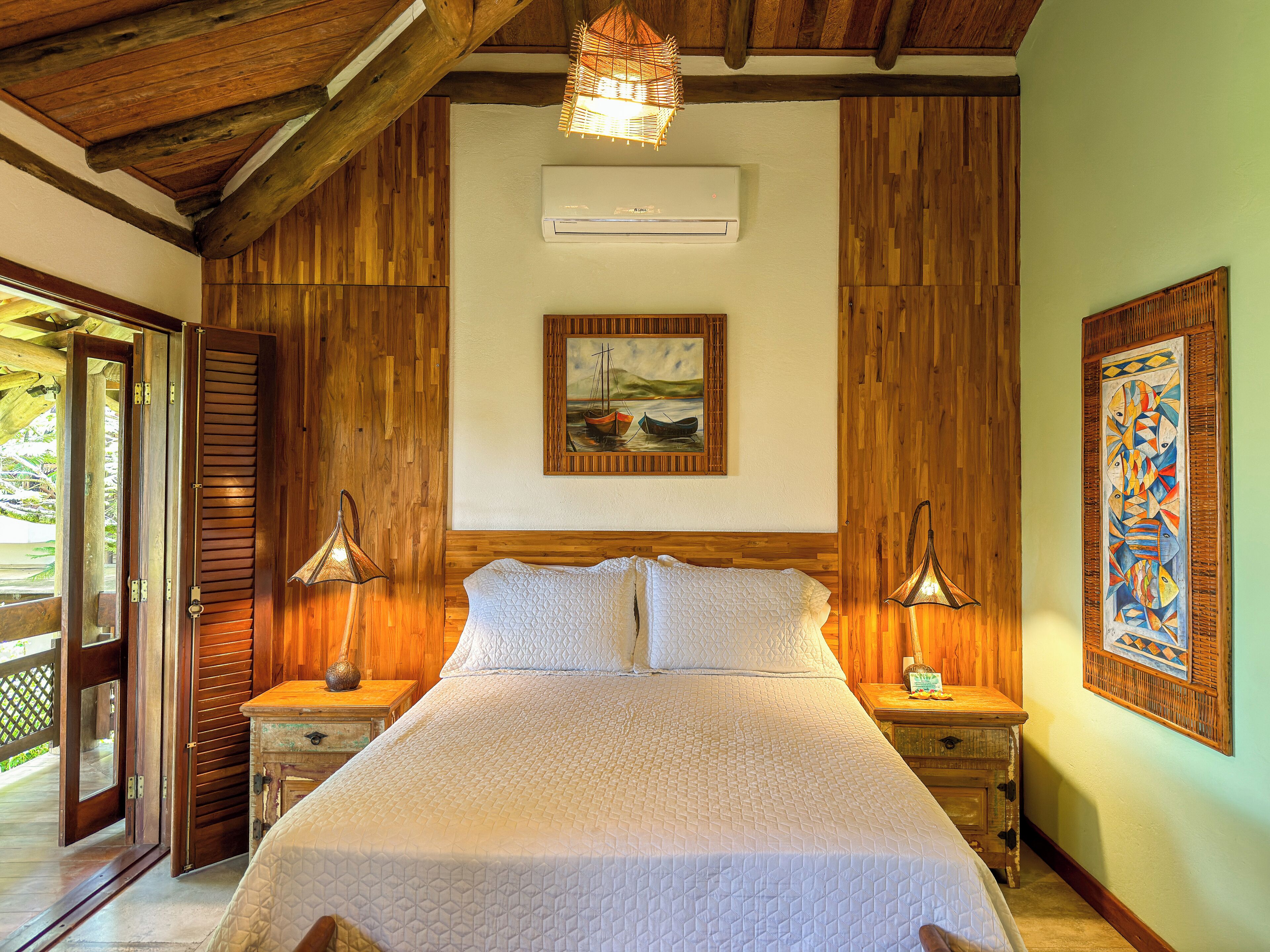 A bedroom with a wooden ceiling, a bed with white bedding, two bedside lamps, and a painting on the wall.