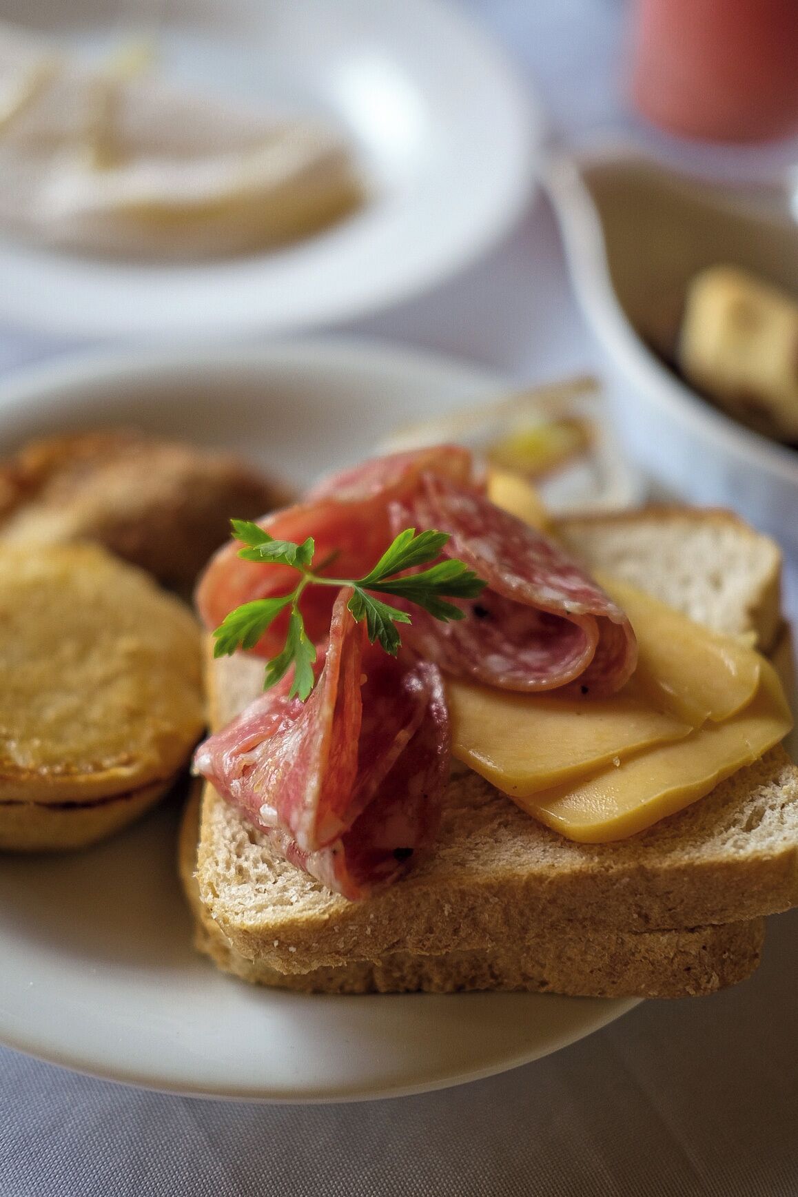 A sandwich with ham and cheese on a slice of bread, accompanied by a small pastry and a sprig of parsley.