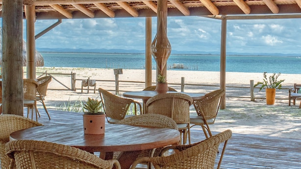 An outdoor wooden deck with wicker furniture and a view of the beach and ocean. - Pousada Barrabella (Maraú)