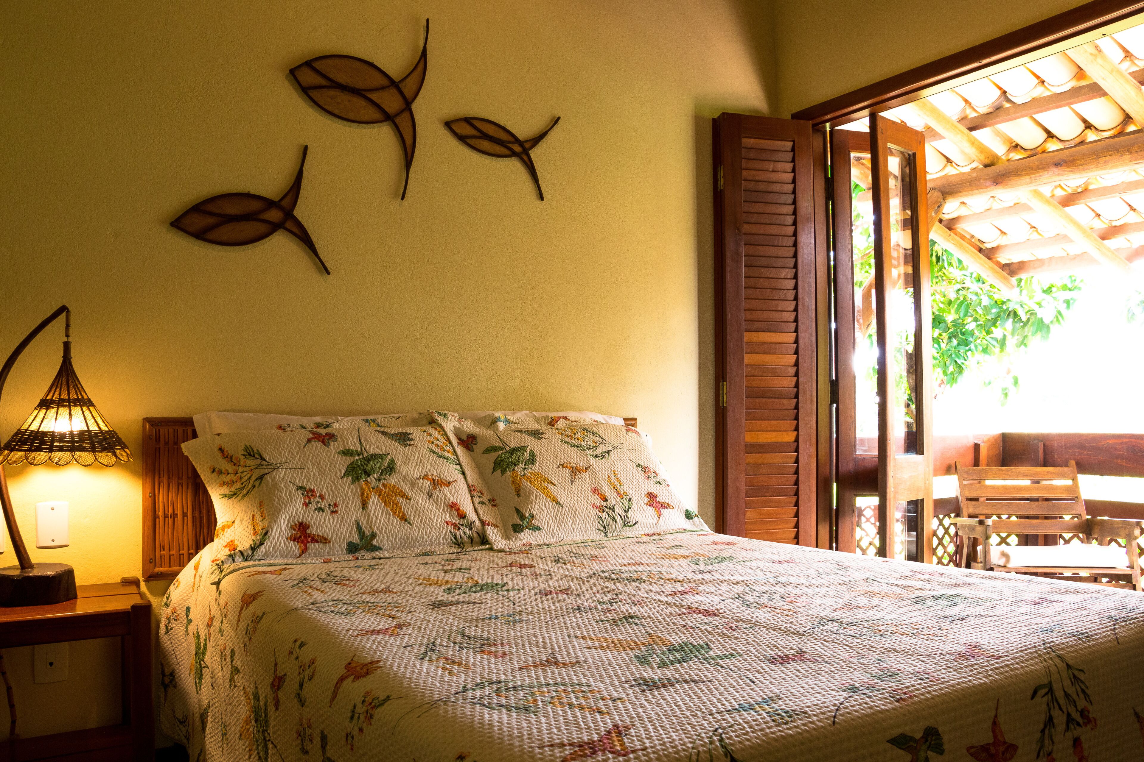 Un lit avec une literie à motifs floraux, un décor mural représentant des poissons et une porte en bois donnant sur un espace extérieur.