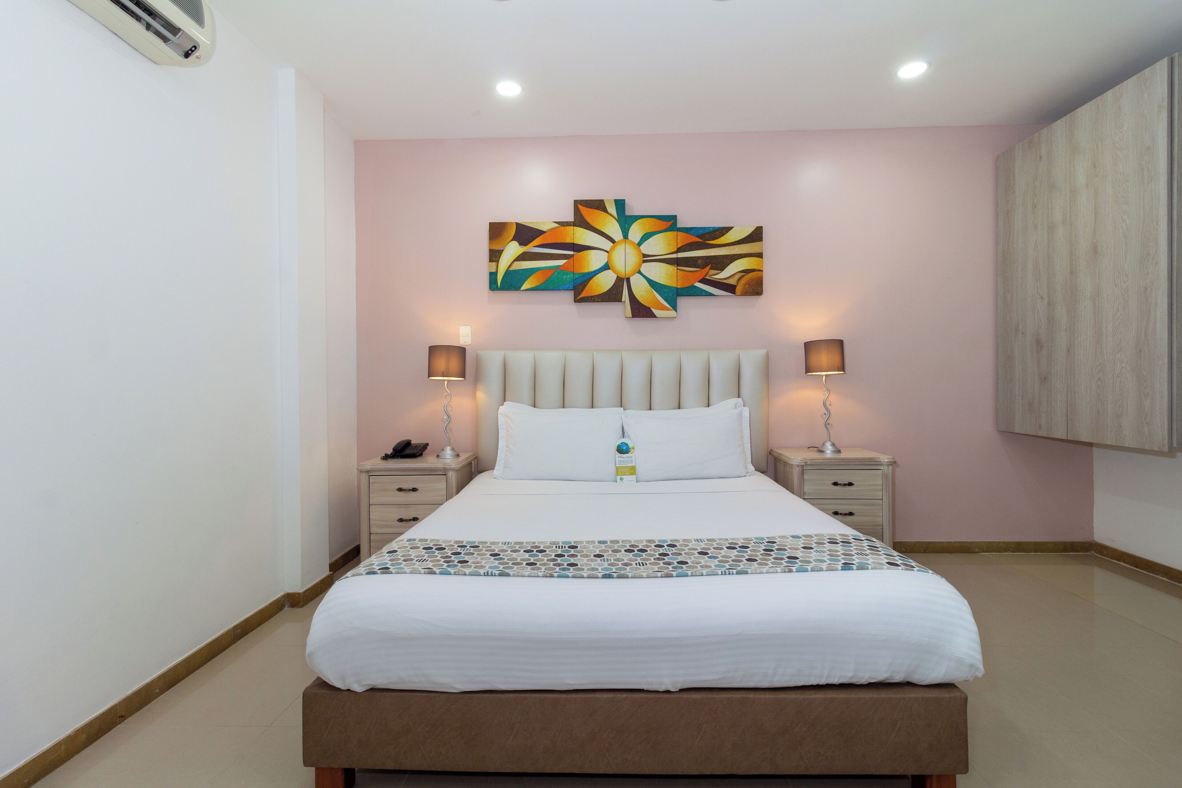 A neatly arranged bedroom with a bed, bedside tables, and a wall-mounted artwork.