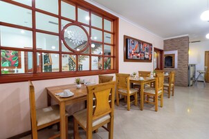 A dining area with wooden tables and chairs, a large window with a circular design, and artwork on the walls.