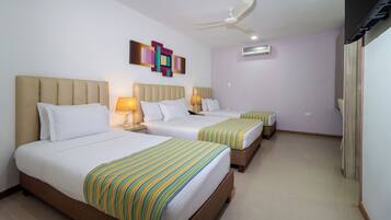 Habitación de hotel con dos camas, ventilador de techo, equipo de aire acondicionado y un cuadro abstracto de colores en la pared.