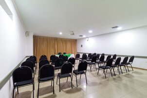 Un salón de conferencias con filas de sillas, un proyector y una mesa con mantel verde.