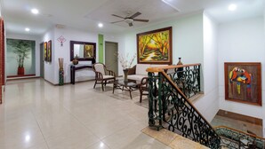A spacious living area with a staircase, a ceiling fan, and a painting of a forest scene.