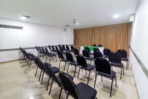 Un salón de conferencias con filas de sillas negras, una mesa verde y un telón de fondo.