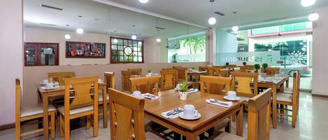 Un comedor con mesas y sillas de madera, un ventanal con vista a palmeras y un letrero que dice "Restaurante".