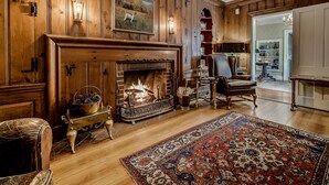 Un salon chaleureux avec une cheminée, des boiseries, un tapis à motifs et un coin repas agrémenté d’un lustre.