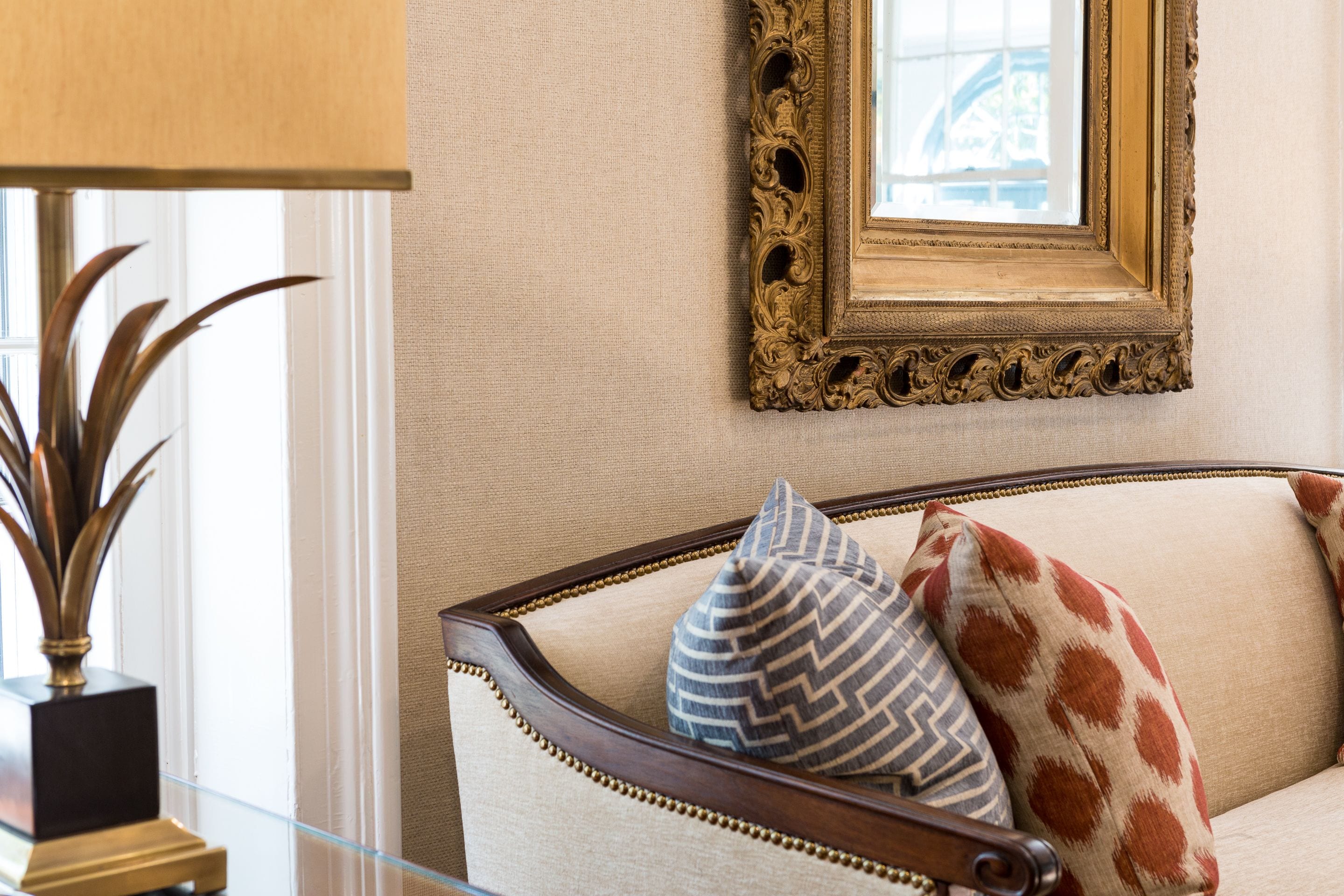 A room with a sofa, decorative pillows, a framed mirror, and a potted plant.