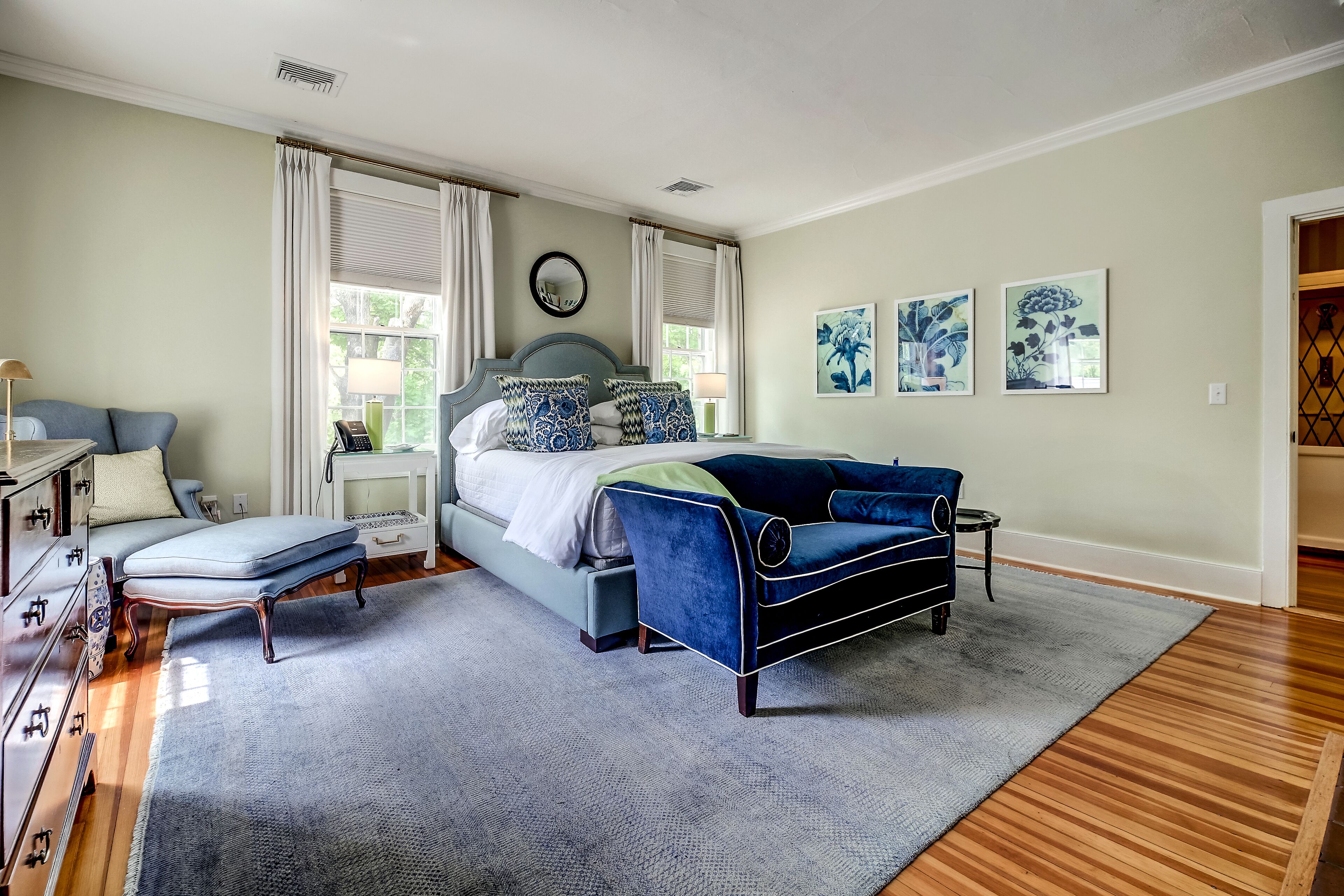 A bedroom with a bed, a blue sofa, a nightstand, a dresser, and a window with curtains.