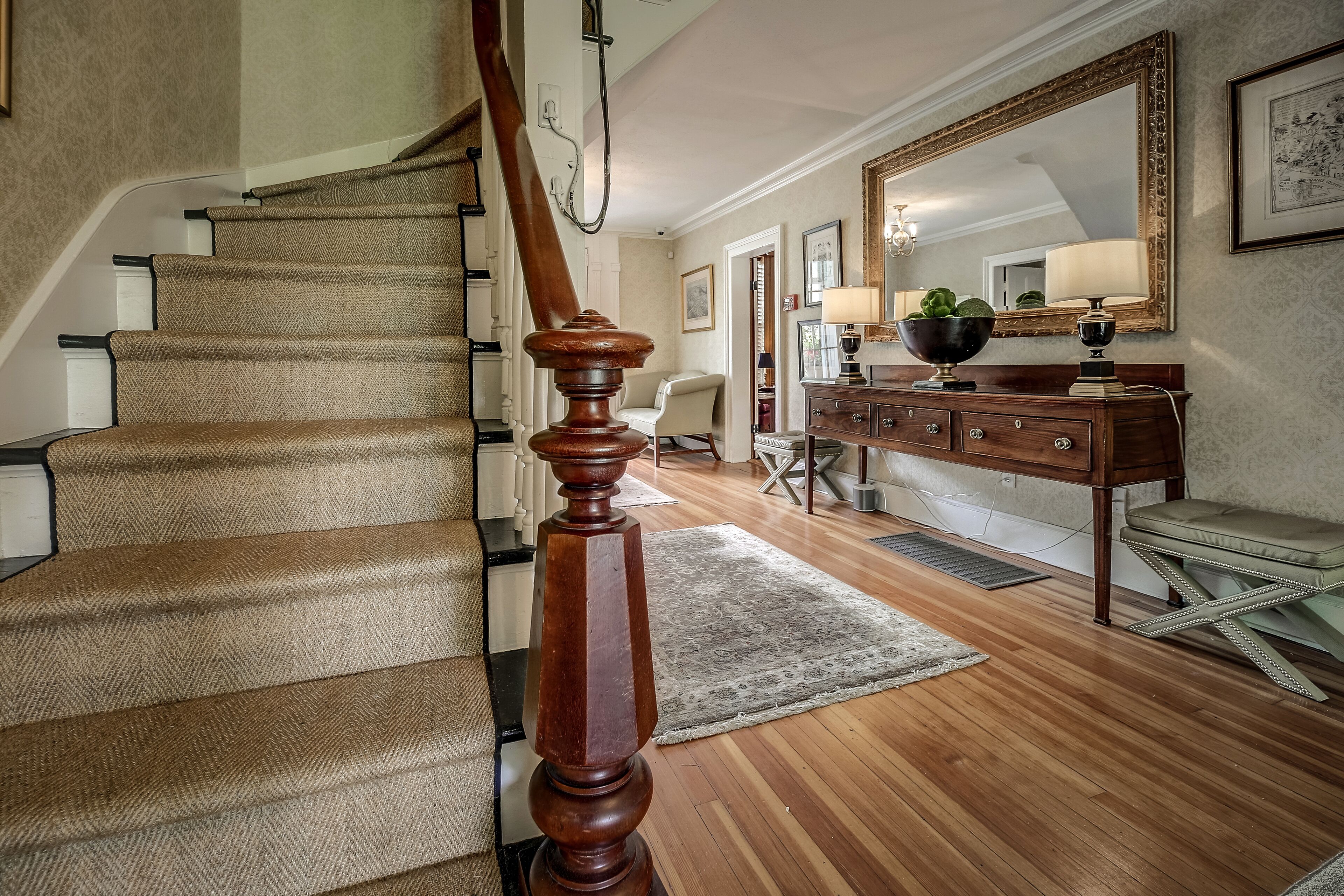 A staircase with a wooden handrail, a wooden bench, and a mirror on the wall.