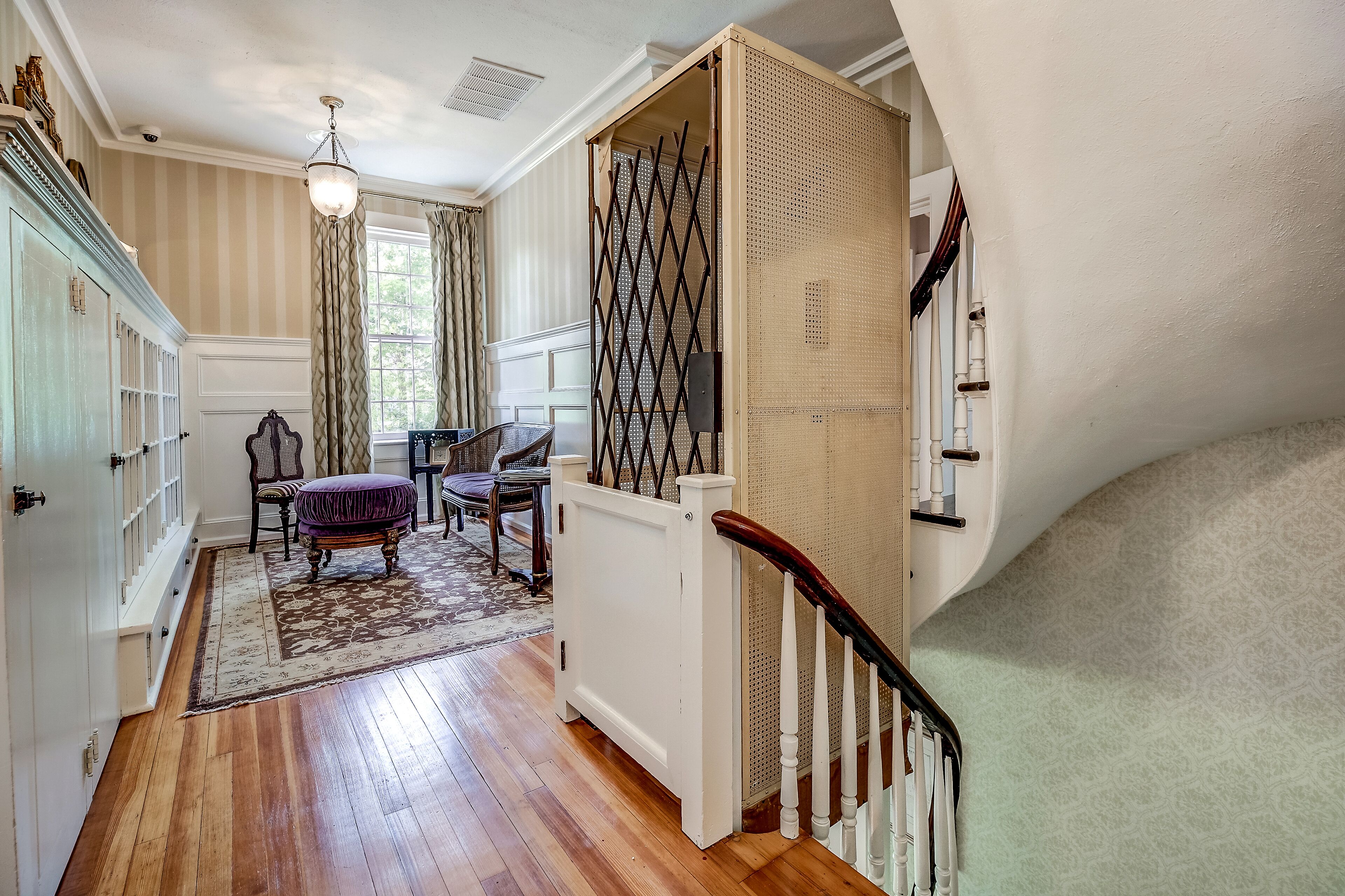 A spacious hallway with wooden flooring, a dining area with a table and chairs, and a staircase with a railing.