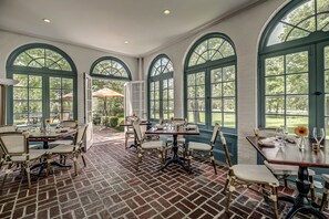 A dining area with brick flooring, large arched windows, and outdoor seating visible through the windows. - Stagecoach Inn (Goshen)