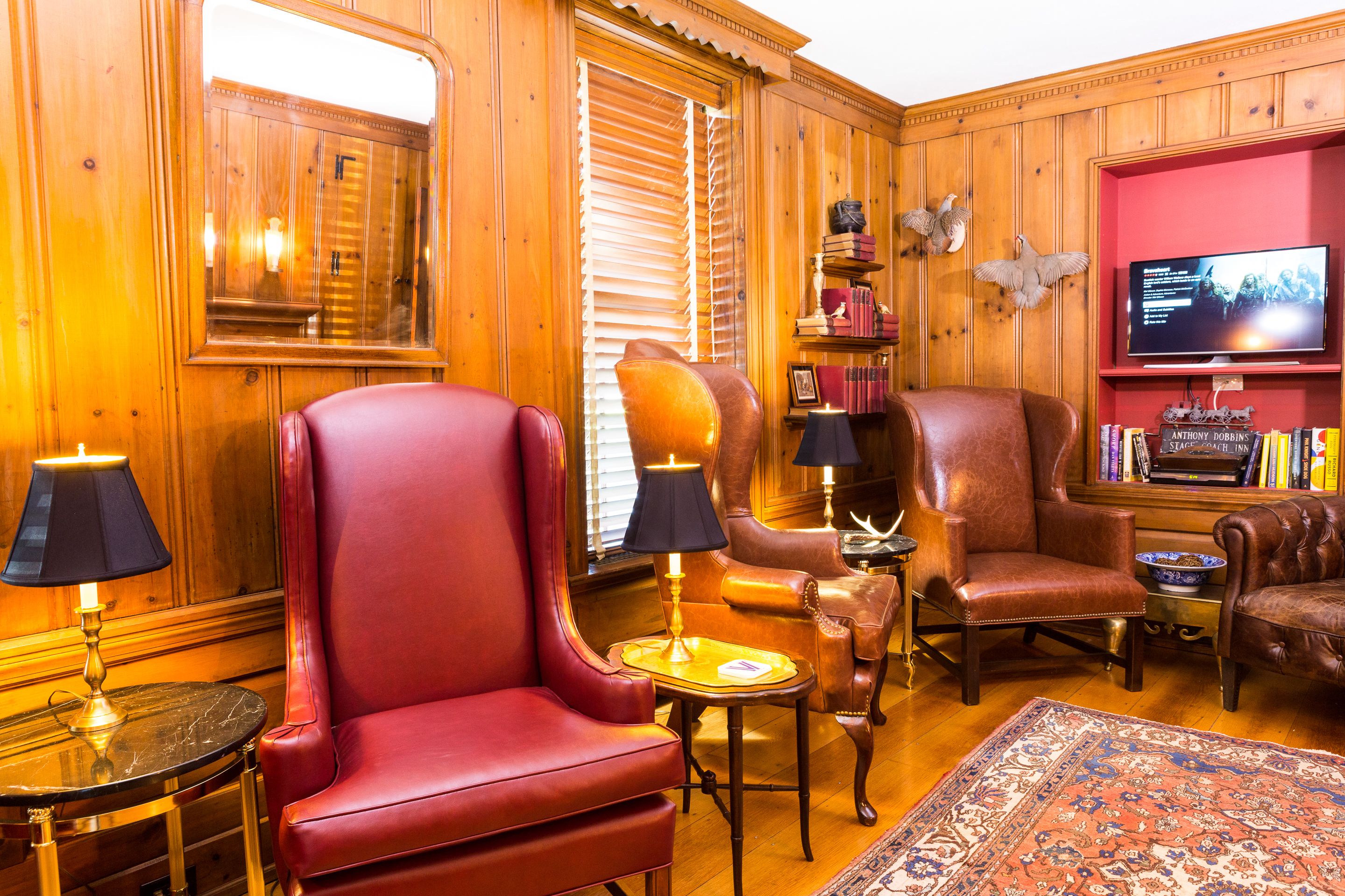 A cozy room with wooden paneled walls, leather armchairs, a television, and a bookshelf.