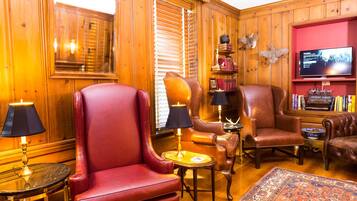 A cozy room with wooden paneled walls, leather armchairs, a television, and a bookshelf.
