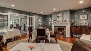 Un coin repas agrémenté d’une cheminée, de nappes blanches et d’une variété d’assiettes décoratives accrochées aux murs.