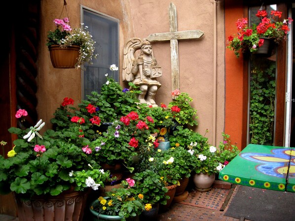 Un patio con plantas en macetas, una estatua de ángel de piedra y una cruz de madera.