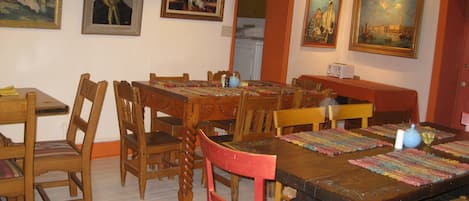 Un comedor con mesas y sillas de madera, un mantel con estampado y una lámpara de vitral.