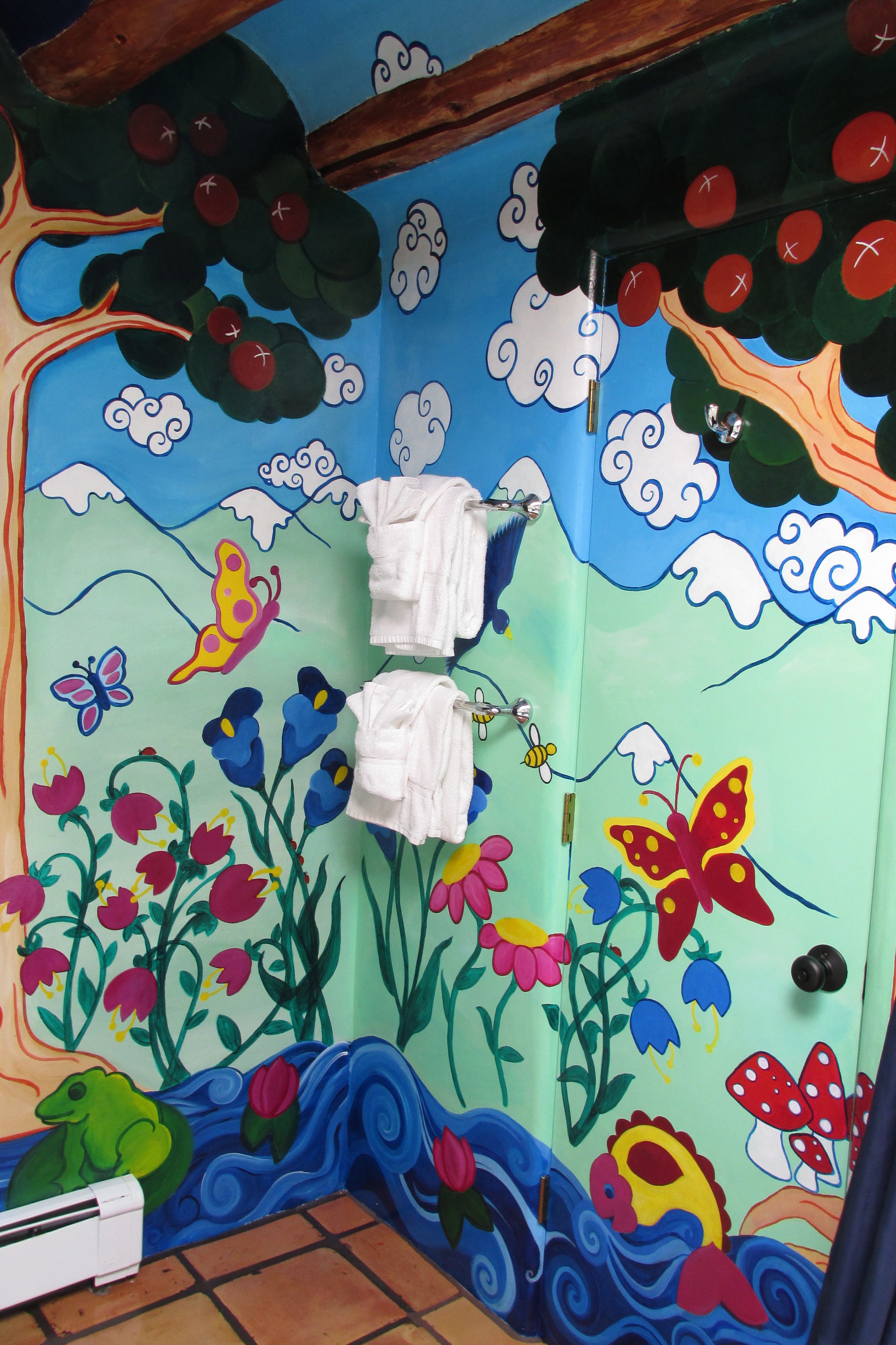 A bathroom with a colorful mural featuring flowers, butterflies, and a frog. There are two white towels hanging on a rack.
